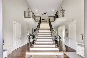 A grand staircase with a black railing, white walls, and a ceiling fan. - Lake Access Mansion w/ Lake View + Theatre + Fire Pit (Heath)