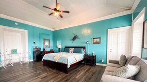A bedroom with a bed, a ceiling fan, a nightstand, a chair, and a couch. - 3rd floor unit with Picturesque Ocean View and outdoor seating! (Frederiksted)