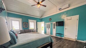 A bedroom with a bed, a ceiling fan, a TV, and a door. - 3rd floor unit with Picturesque Ocean View and outdoor seating! (Frederiksted)