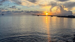 A sunset over a calm body of water with a pier extending into the water. - 3rd floor unit with Picturesque Ocean View and outdoor seating! (Frederiksted)