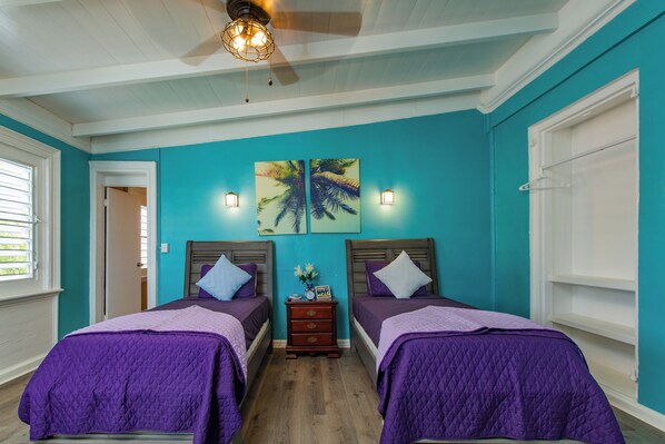 A room with two beds, teal walls, and a ceiling fan.