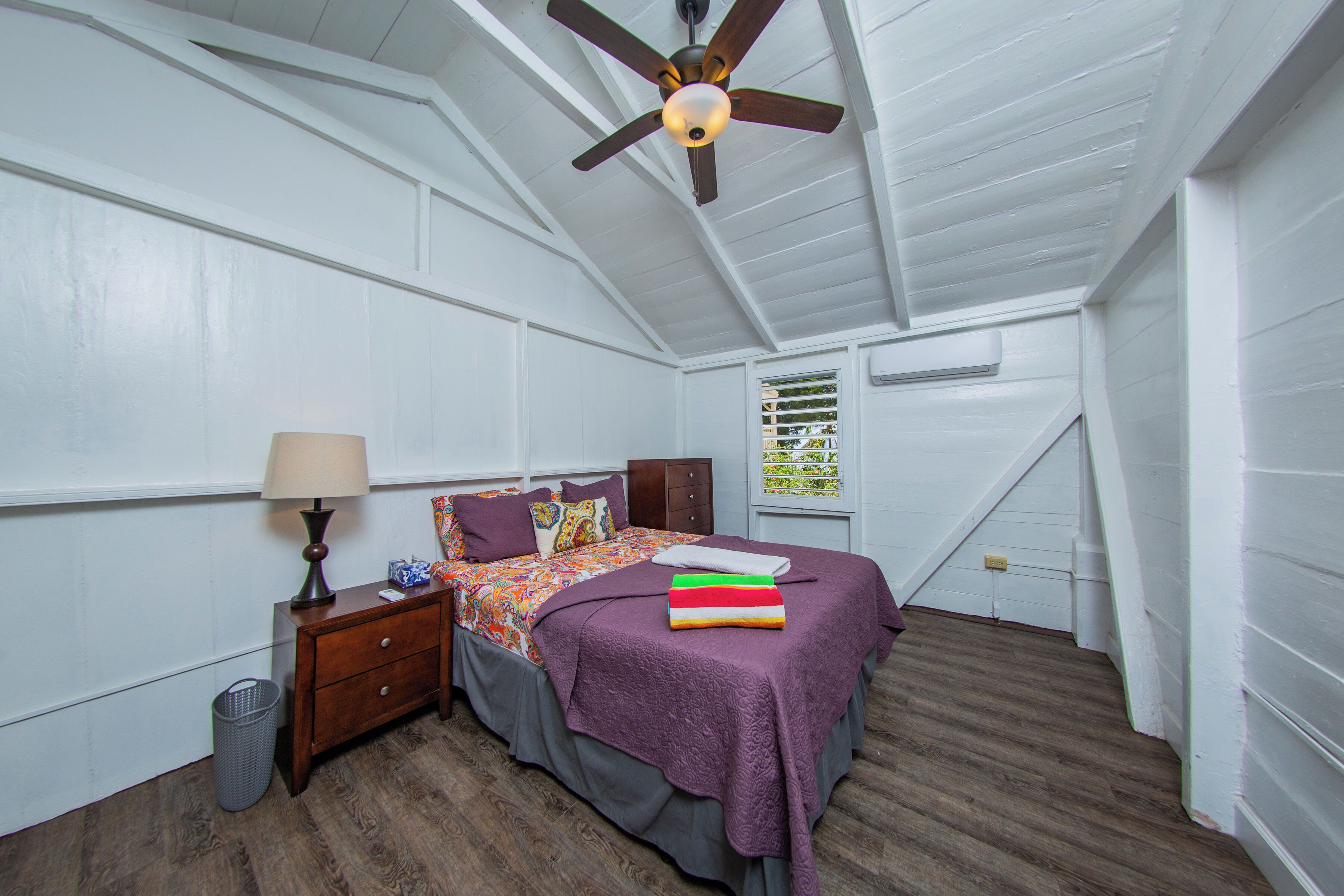 A bedroom with a bed, nightstand, lamp, and a ceiling fan.
