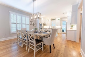 A dining area with a wooden table, white chairs, and a hanging light fixture. - Honey's Haven | Luxury St. Simons Island Vacation Rental with Private Pool Near Pier Village (St. Simons Island)