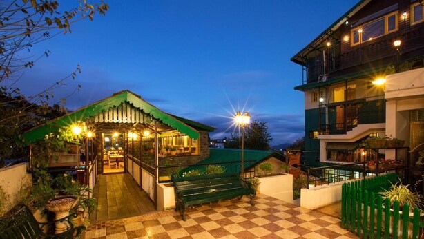 A courtyard with a checkered floor, a green-roofed structure, and a multi-story building with balconies. - Pine Borough Inn (Kodaikanal)