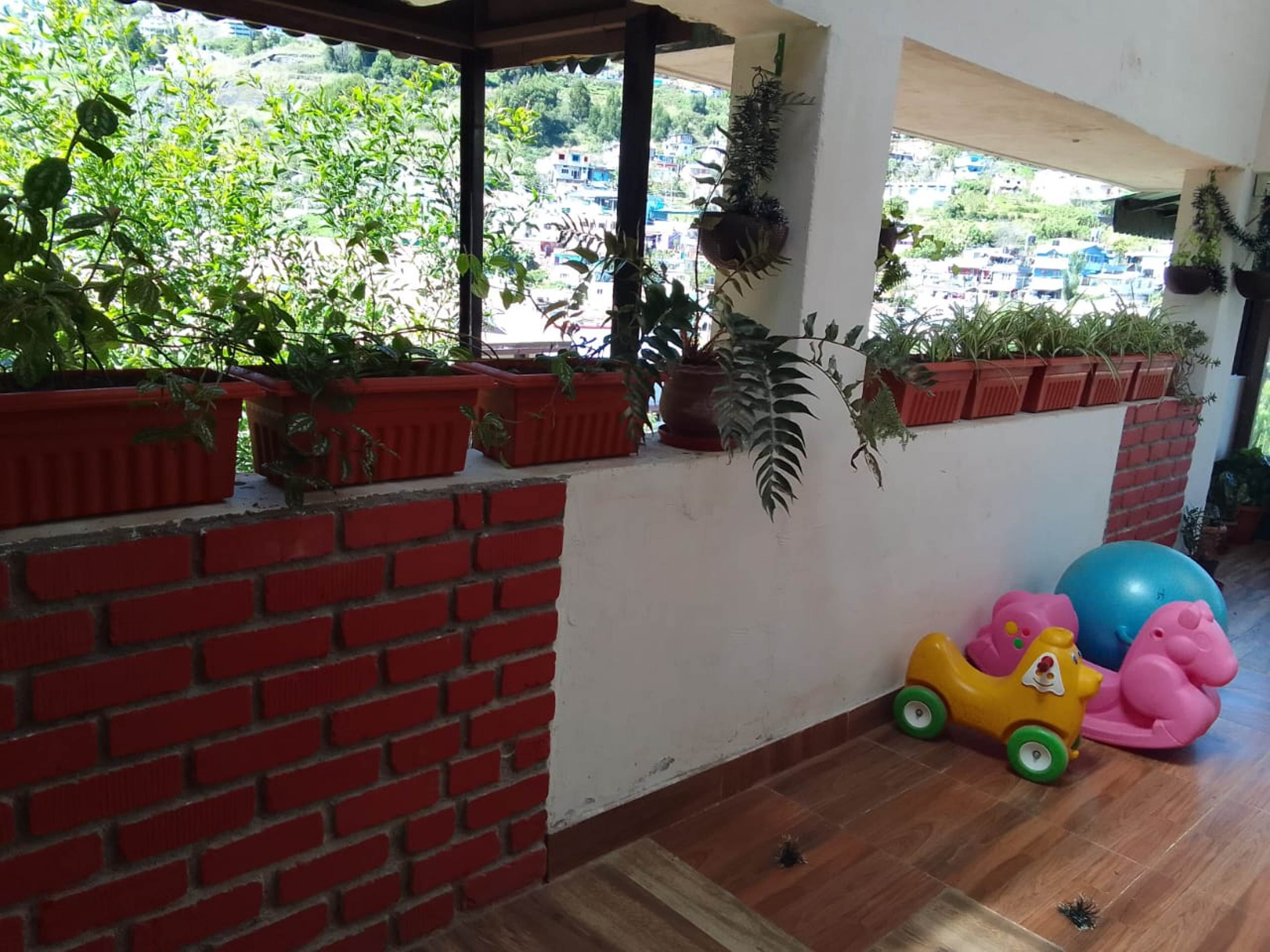 A room with a brick wall, potted plants, a yellow toy car, and exercise balls.