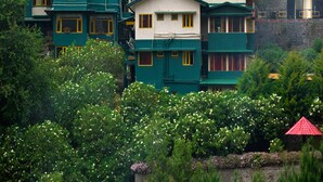 A cluster of multi-story buildings with a mix of green and white exteriors, surrounded by lush greenery and flowering plants. - Pine Borough Inn (Kodaikanal)