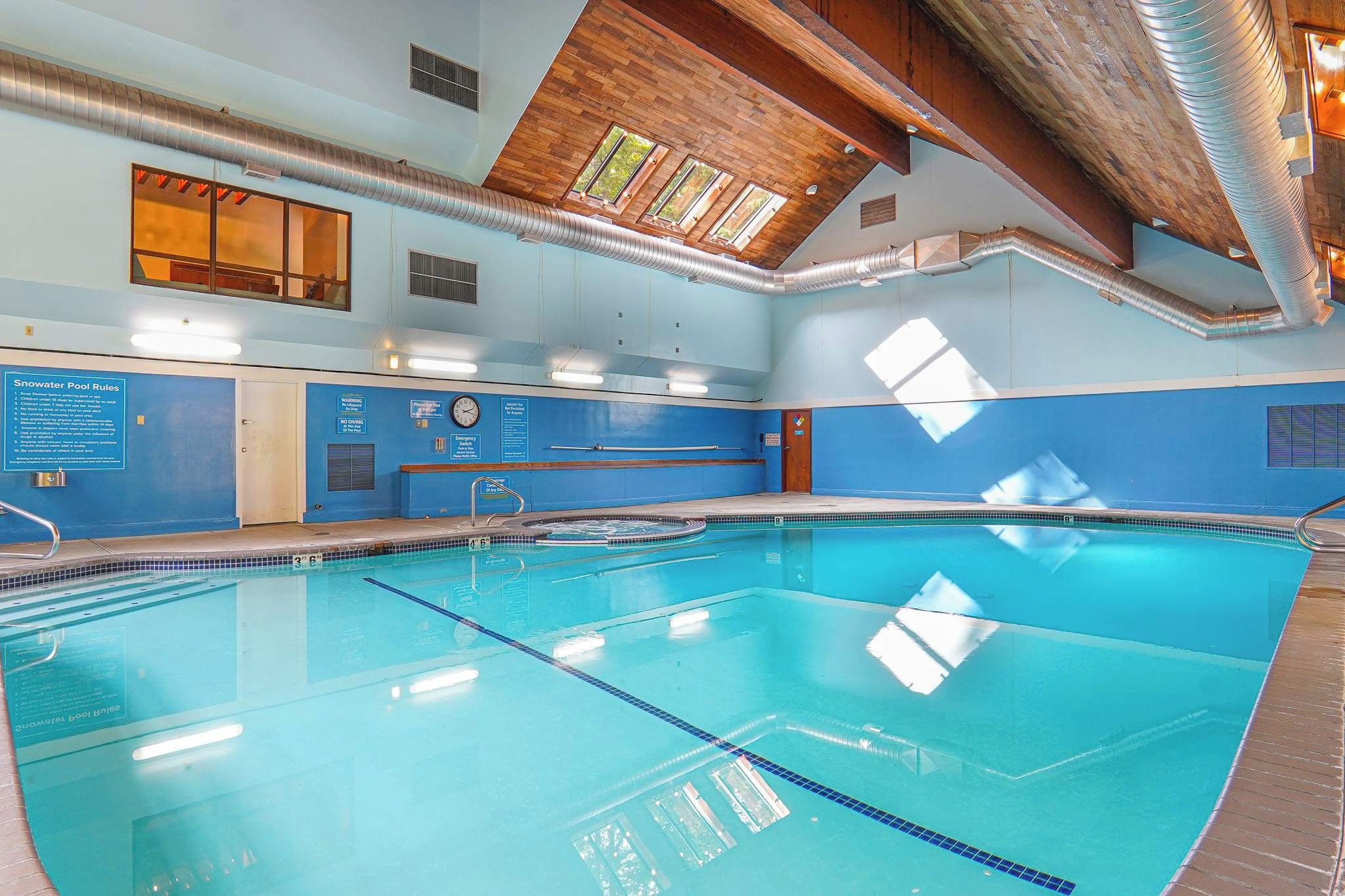 An indoor swimming pool with clear water, marked lanes, and a wooden ceiling.