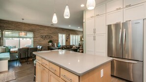 A modern kitchen with a large island, stainless steel appliances, and a dining area with a sofa and chairs. - Luxe Scottsdale Home W/pool, Spa, & Tesla Charger (Scottsdale)