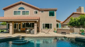 A two-story house with a swimming pool, a patio with outdoor furniture, and a covered entryway.