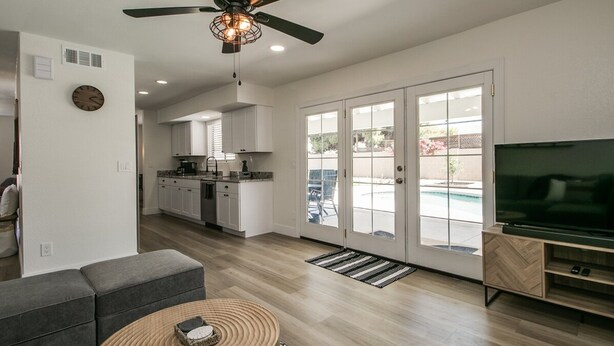 A modern living room with a grey sofa, a TV, and a ceiling fan. - Upgraded 4-bdrm Beautiful Home W/pool! (Glendale)