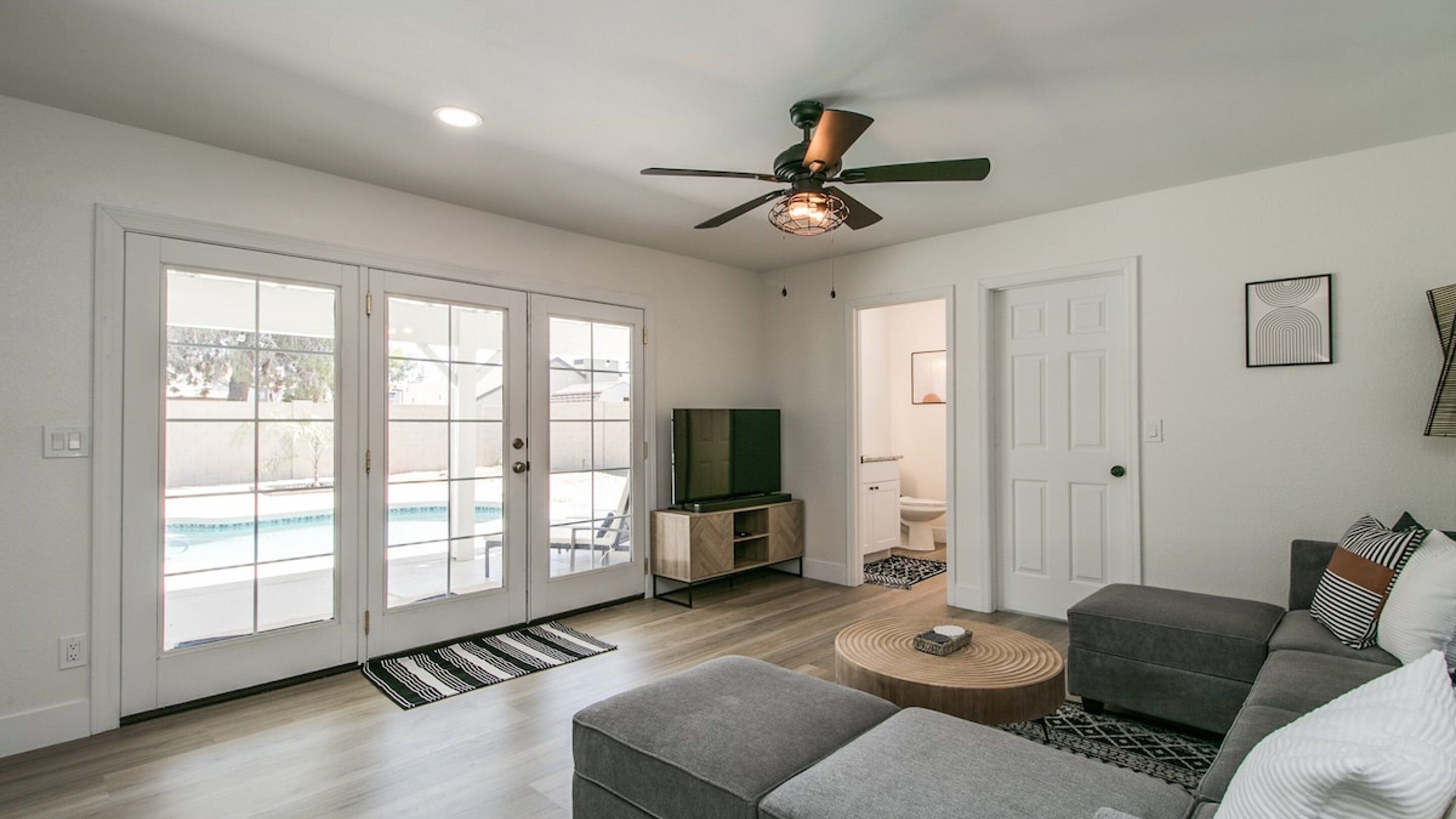 A spacious living room with a grey sofa, a coffee table, and a ceiling fan.