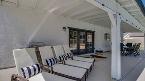 A covered outdoor seating area with white cushioned chairs and striped pillows, a grill, and a door leading to a patio with a table and chairs. - Upgraded 4-bdrm Beautiful Home W/pool! (Glendale)