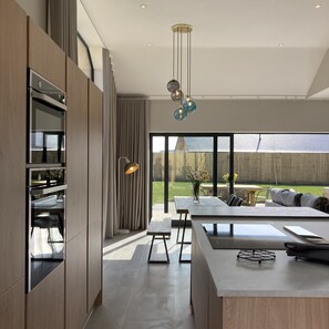 Een moderne keuken met inbouwapparatuur, een eethoek met een grote tafel en uitzicht op de achtertuin.