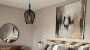 Une chambre à coucher comprenant un lit, un bureau, une chaise, un luminaire suspendu et un tableau accroché au mur.