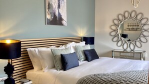 Une chambre à coucher bien rangée, avec un lit, des tables de chevet, une lampe, un miroir fixé au mur et un tableau.