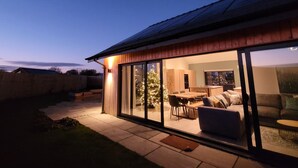 Une maison moderne dotée d’un patio entièrement vitré, d’une terrasse en bois et d’un sapin de Noël.