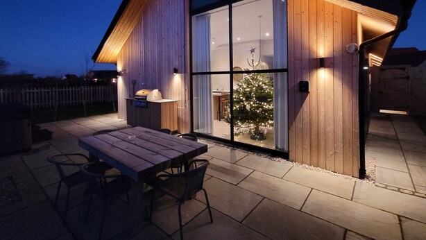 Une maison moderne en bois, dotée d’un patio, d’une table à manger et d’un sapin de Noël.
