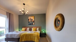 Une chambre moderne avec un grand lit, des tables de chevet, un lustre, des œuvres d’art et un miroir.