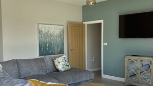 Un salon avec un canapé gris, une table basse ronde, un téléviseur à écran plat et un élément décoratif mural.