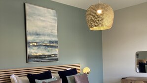 A bedroom with a bed, pillows, a blanket, a hanging light fixture, a painting, and a bedside table. - Water Lily Cottage, Ashlin Farm Barns (Lincoln)