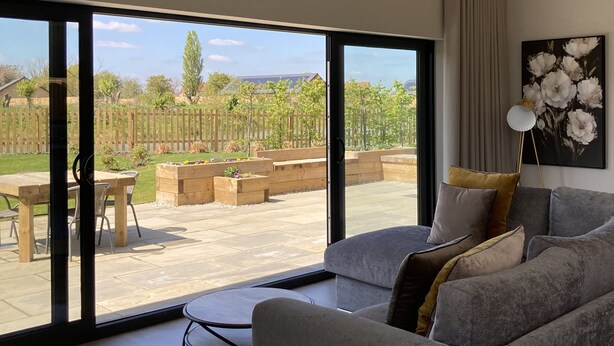 A modern living room with a large sliding glass door leading to an outdoor patio. - Water Lily Cottage, Ashlin Farm Barns (Lincoln)