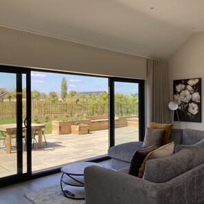 A modern living room with a large sliding glass door leading to an outdoor patio. - Water Lily Cottage, Ashlin Farm Barns (Lincoln)