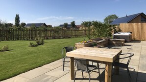A patio area with a wooden table and chairs, a hot tub, and a wooden fence in the background. - Water Lily Cottage, Ashlin Farm Barns (Lincoln)