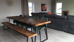 A modern living room with a wooden dining table, green upholstered chairs, a grey sofa with orange cushions, and a large abstract painting on the wall. - Chestnut House, Ashlin Farm Barns (Lincoln)