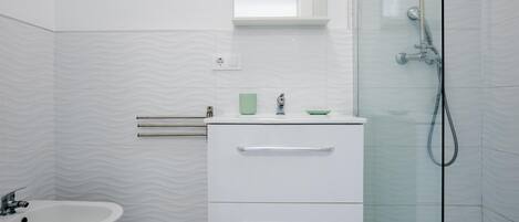 A modern bathroom with a bidet, a sink, and a glass shower enclosure.
