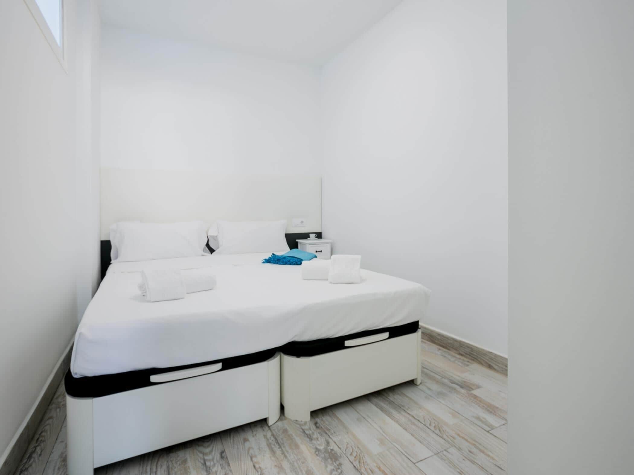 A small, modern bedroom with a single bed, white bedding, and a nightstand with a lamp.