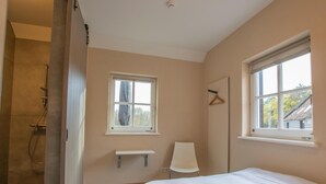 Een slaapkamer met een bed, een raam, een stoel en een klein plankje.