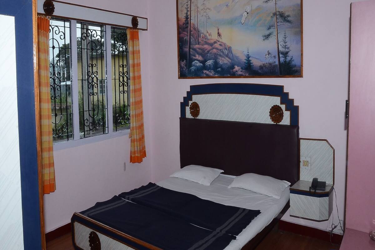 Une chambre à coucher avec un lit, une table de chevet, un tableau et une fenêtre avec des rideaux.