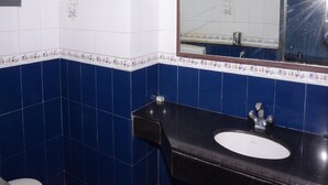 A bathroom with a black sink, white and blue tiles, a towel rack, and a mirror. - Jayaraj Residency (Kodaikanal)