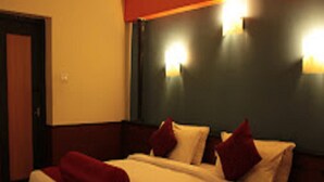 A hotel room with a double bed, two pillows, a red throw blanket, and two wall-mounted lights. - Jayaraj Residency (Kodaikanal)
