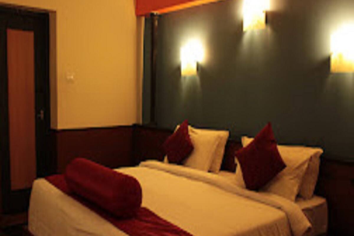 Une chambre d’hôtel avec un lit double, deux oreillers, un plaid rouge et deux lampes fixées au mur.