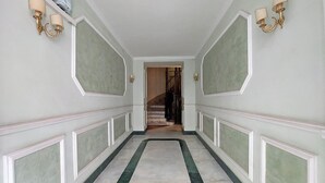 A hallway with a marble floor, white wainscoting, and wall-mounted sconces. - alla locanda Malandra (Rome)