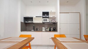 A modern kitchen with white cabinets, a microwave, and a coffee machine. There are two wooden tables with orange chairs. - alla locanda Malandra (Rome)