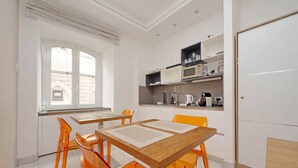 A modern kitchen with white cabinets, a microwave, and a coffee maker. There are orange chairs around a wooden table. - alla locanda Malandra (Rome)
