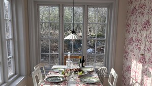 Comedor con una mesa lista para cuatro, ventanas amplias y un ventilador de techo.