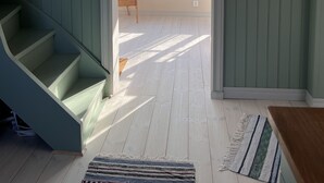 Una escalera conduce a una habitación luminosa con un ventanal grande, un cuadro enmarcado en la pared y una silla de mimbre cerca de la ventana.