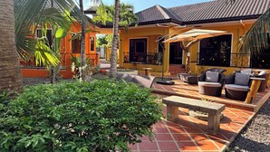A courtyard with outdoor seating, palm trees, and a building with a tiled roof. - Alona's Coral Garden Resort  (Panglao)