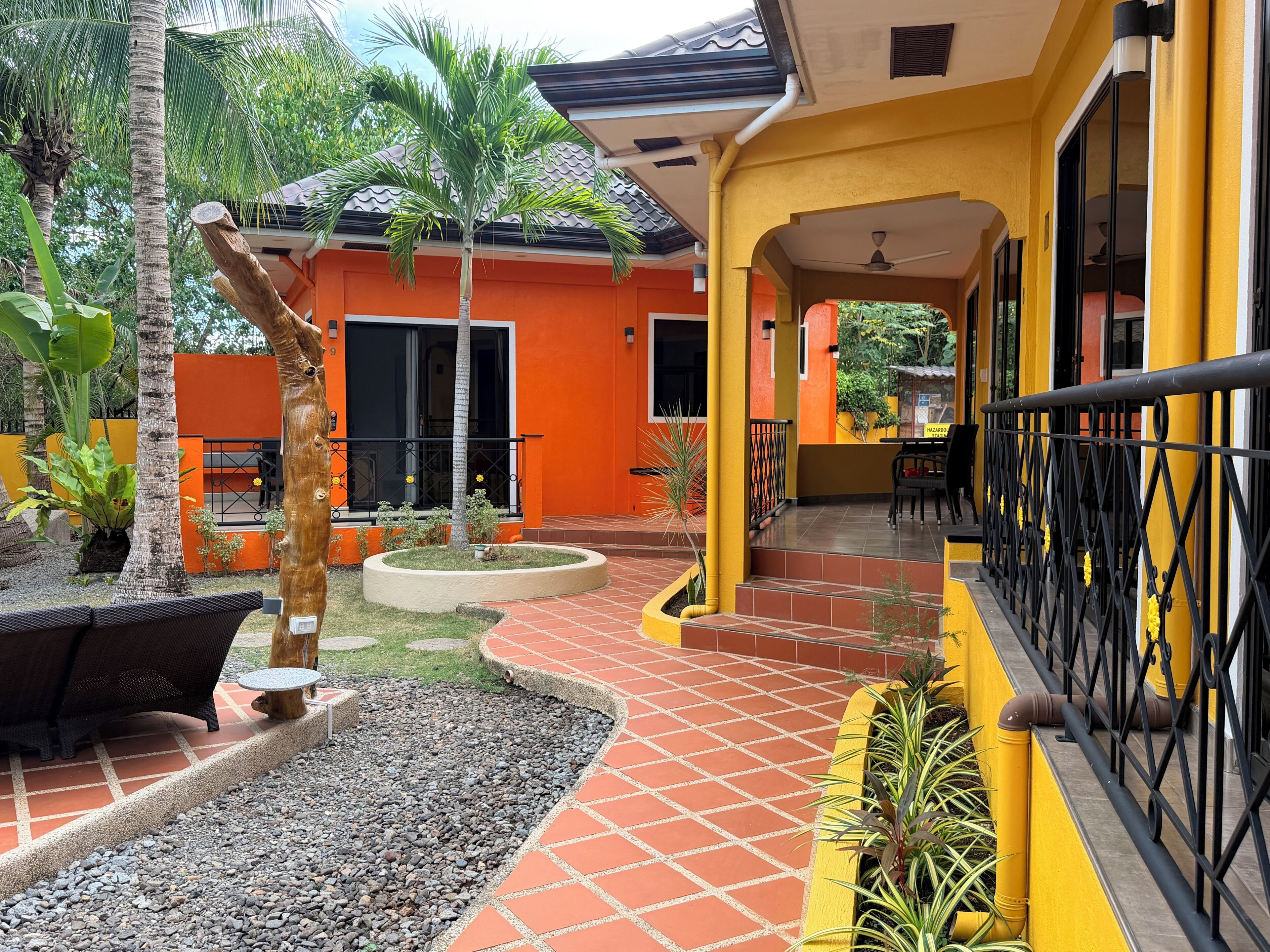 A courtyard with a palm tree, outdoor seating, and a yellow building with a tiled floor.