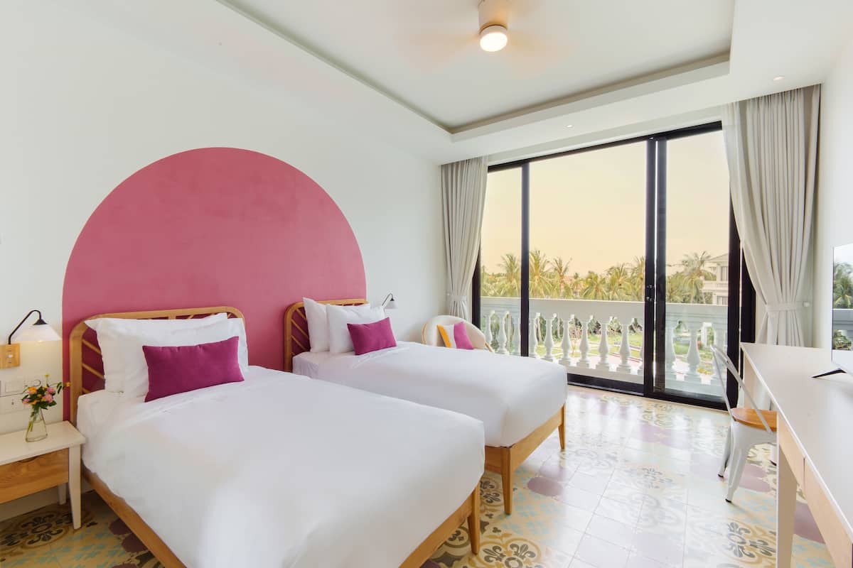 A hotel room with two beds, a large window, a balcony, and a desk.