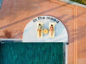 Deux personnes se prélassent au soleil au bord d’une piscine, et un panneau indique : « envie de se détendre ».