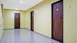 A hallway with three wooden doors, each marked with a number. The walls are painted yellow, and the floor is tiled. - Hotel Carnival (Rajgurunagar)