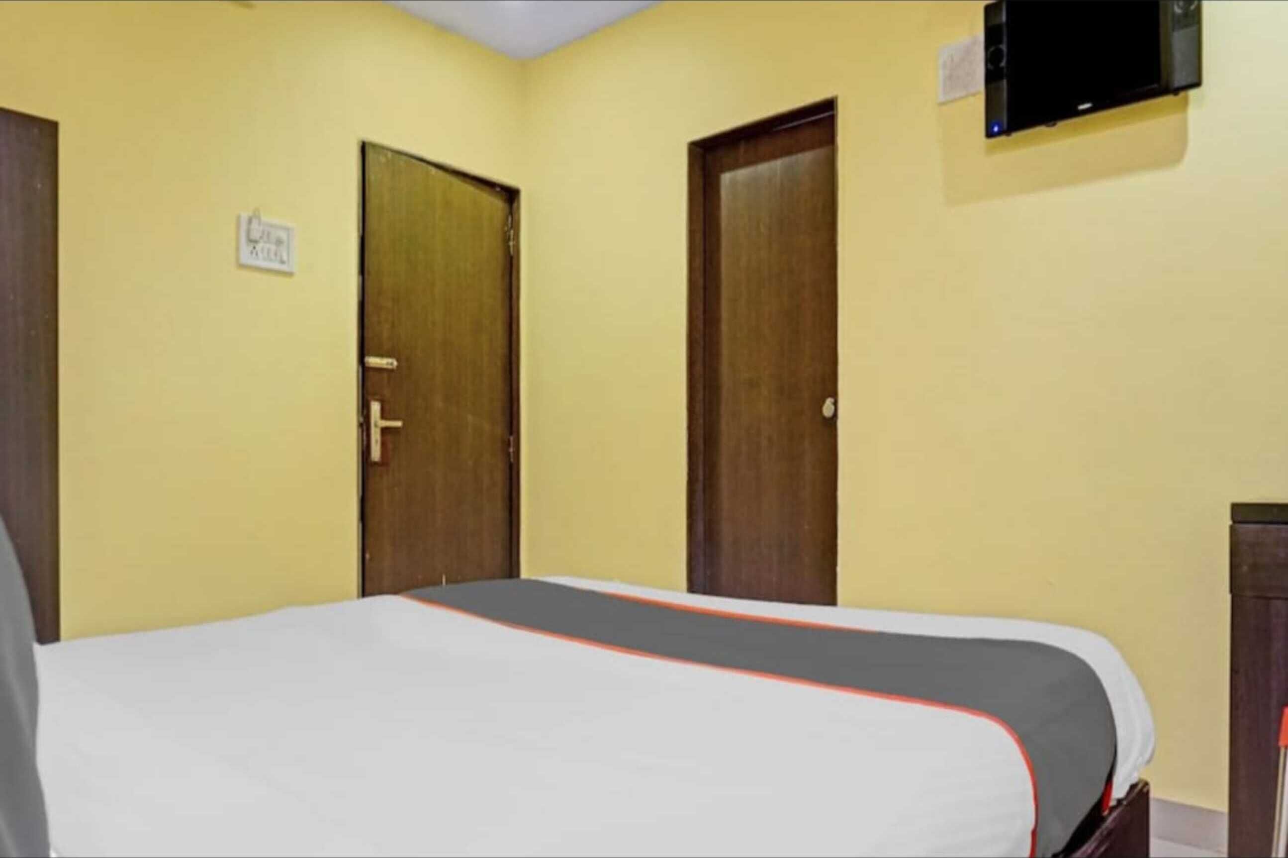 Habitación de hotel con una cama, dos puertas, un televisor montado en la pared y un letrero que indica el tipo de habitación.