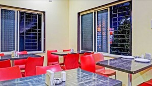 A dining area with red chairs and black tables, large windows with metal grilles, and a view of the outside. - Hotel Carnival (Rajgurunagar)