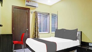 A hotel room with a bed, a desk, a chair, and a window with curtains. - Hotel Carnival (Rajgurunagar)
