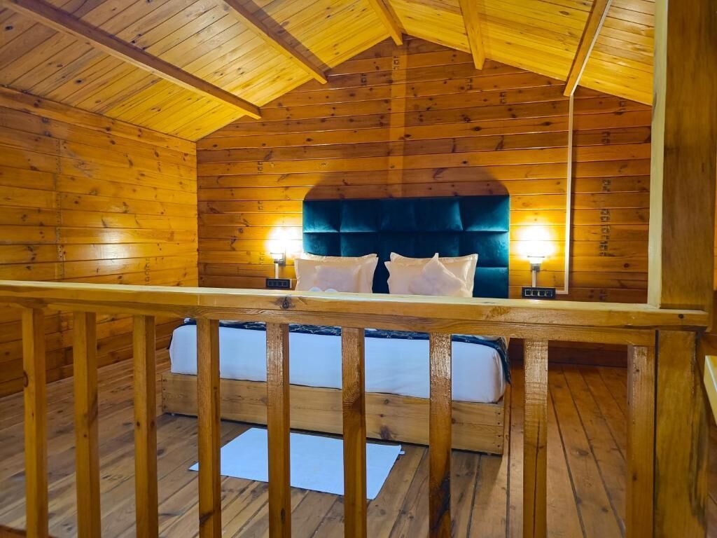 A wooden cabin room with a bed, two bedside lamps, and a wooden railing.