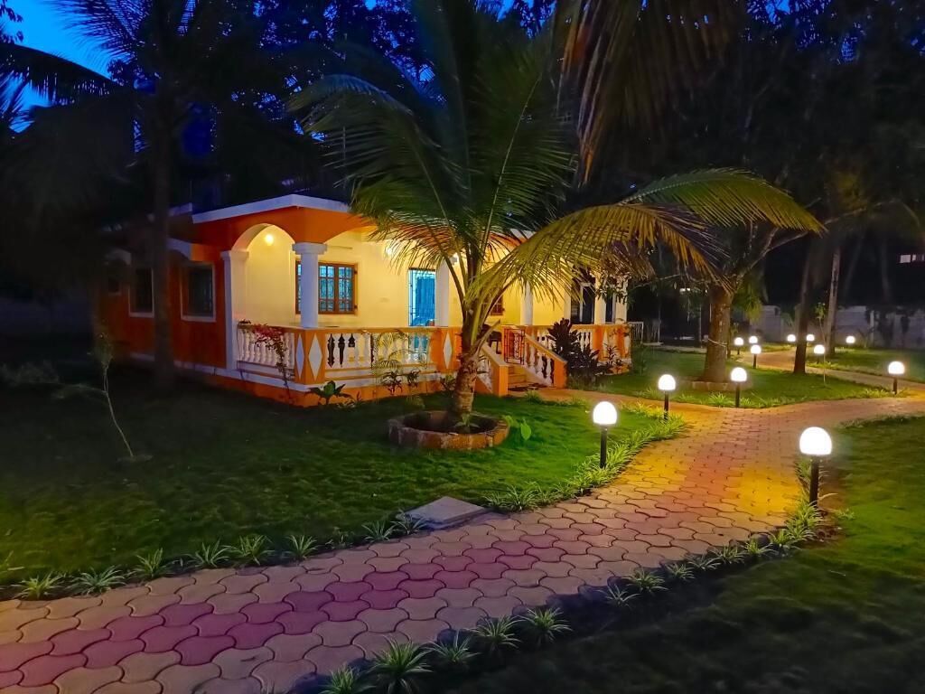 A well-lit building with a paved pathway leading to a covered area, surrounded by greenery and palm trees.